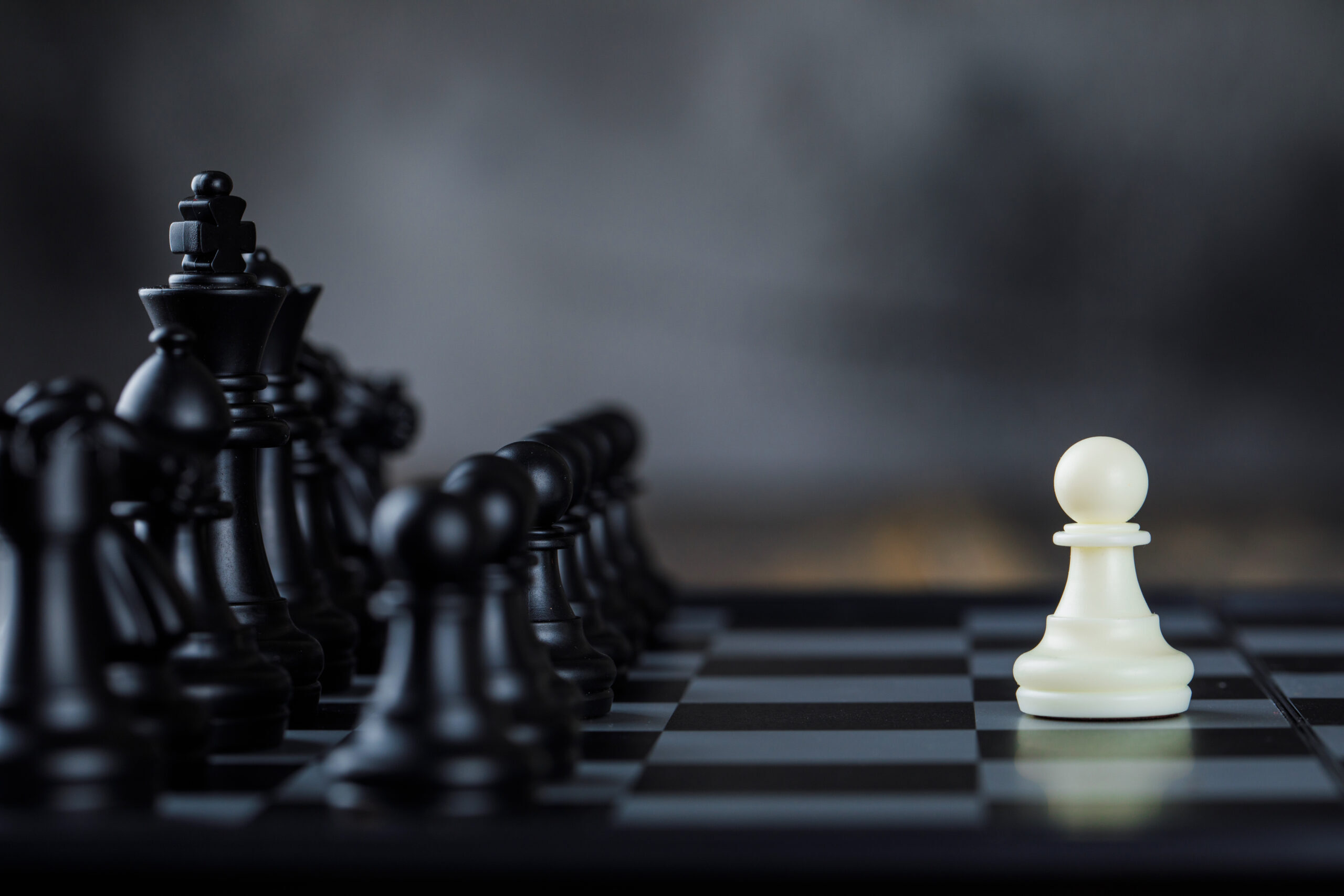 Business strategy concept with figures on chessboard on foggy and wooden background side view.